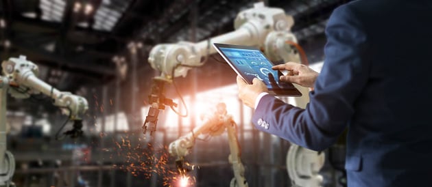 A manager industrial engineer uses real-time monitoring system software to check and control 5G enabled robots on the factory floor.